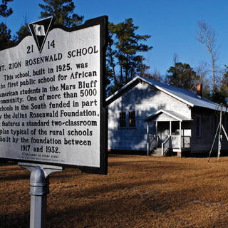 A historical marker for the Mt. Zion Rosenwald School stands in the foreground with the historic white wooden schoolhouse visible in the background.