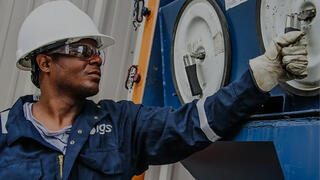 A IGS worker in safety gear operates a lever on a large piece of blue industrial equipment, representing Power and Energy Sector
