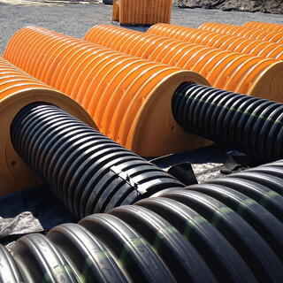 Rows of black corrugated pipes emerge from large, yellow semi-cylindrical structures laid out on the ground, representing building products sector.
